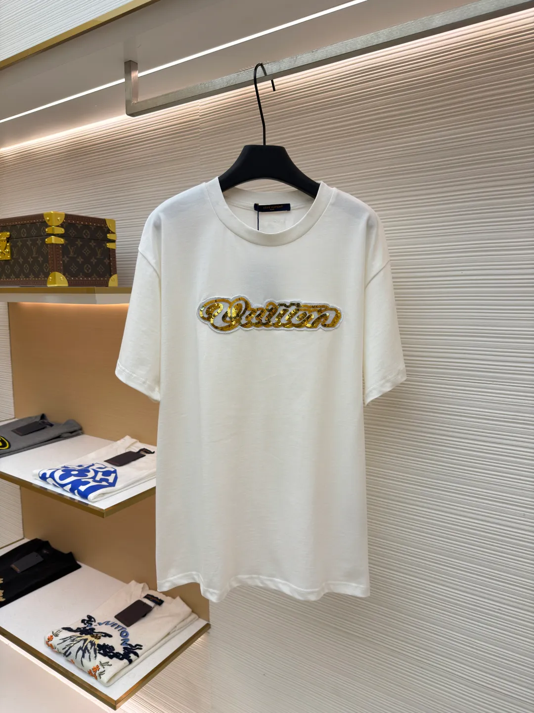 LOUIS VUITTON cotton round neck embroidered Vuitton signature logo short sleeves ●Original version: purchased and developed for 12300 ●Item number: 1682272-A10 ●Fabric: cotton fabric ●Technology: embroidery production ●Color: white ●Version: fitted version ●Weight: about 270 grams ●Size: S-M-L-XL ●Description: This white short-sleeved T-shirt is made of high-count combed cotton fabric and has been treated with pre-washing technology. It has a soft and skin-friendly touch and is not easy to deform. The silhouette of the shirt is a loose shoulder design, which meets the needs of modern casual wear. The core decoration area on the chest uses hand-beading and bronzing technology, and uses metallic gold sequins and embroidery threads intertwined to outline a three-dimensional letter pattern. The sequins are layered and inlaid, and each one is manually positioned and fixed by craftsmen to ensure a regular texture and uniform gloss. The edges of the letters are sewn with matte silk thread to form a visual contrast between gold and matte, while reinforcing the decorative structure to avoid falling off during wear. The neckline uses double-needle hemming technology and is matched with ribbed cuffs of the same fabric. It is durable and fits the neck. The overall craftsmanship combines handicraftsmanship with modern clothing technology, and the details show exquisite texture. The overall wiring is straight and delicate, the fabric is comfortable and soft, and the color is consistent without color difference. It can be matched with the same style to create a fashionable look and control various occasions. Customized accessories, complete with three standards, same style for men and women!